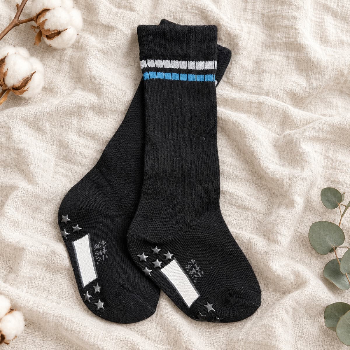 Black knee-high socks with grey and blue stripes and star grips on cream linen with nursery props