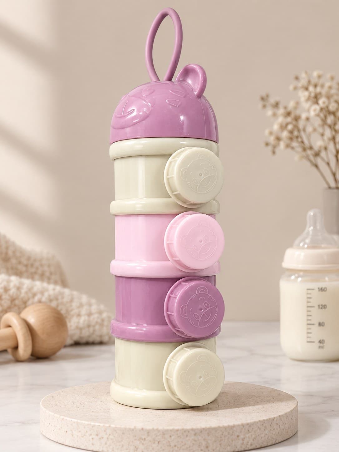Four-tier formula dispenser with a mauve bear lid and carry loop, and cream, pink and mauve layers with screw caps