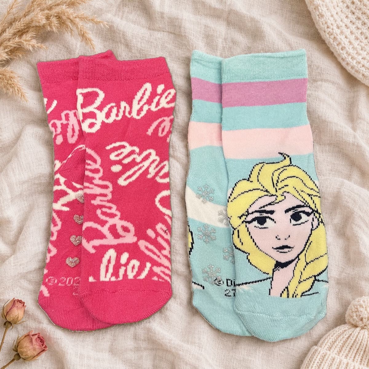 Pink Barbie and aqua Frozen Elsa socks, two pairs on cream linen with nursery props