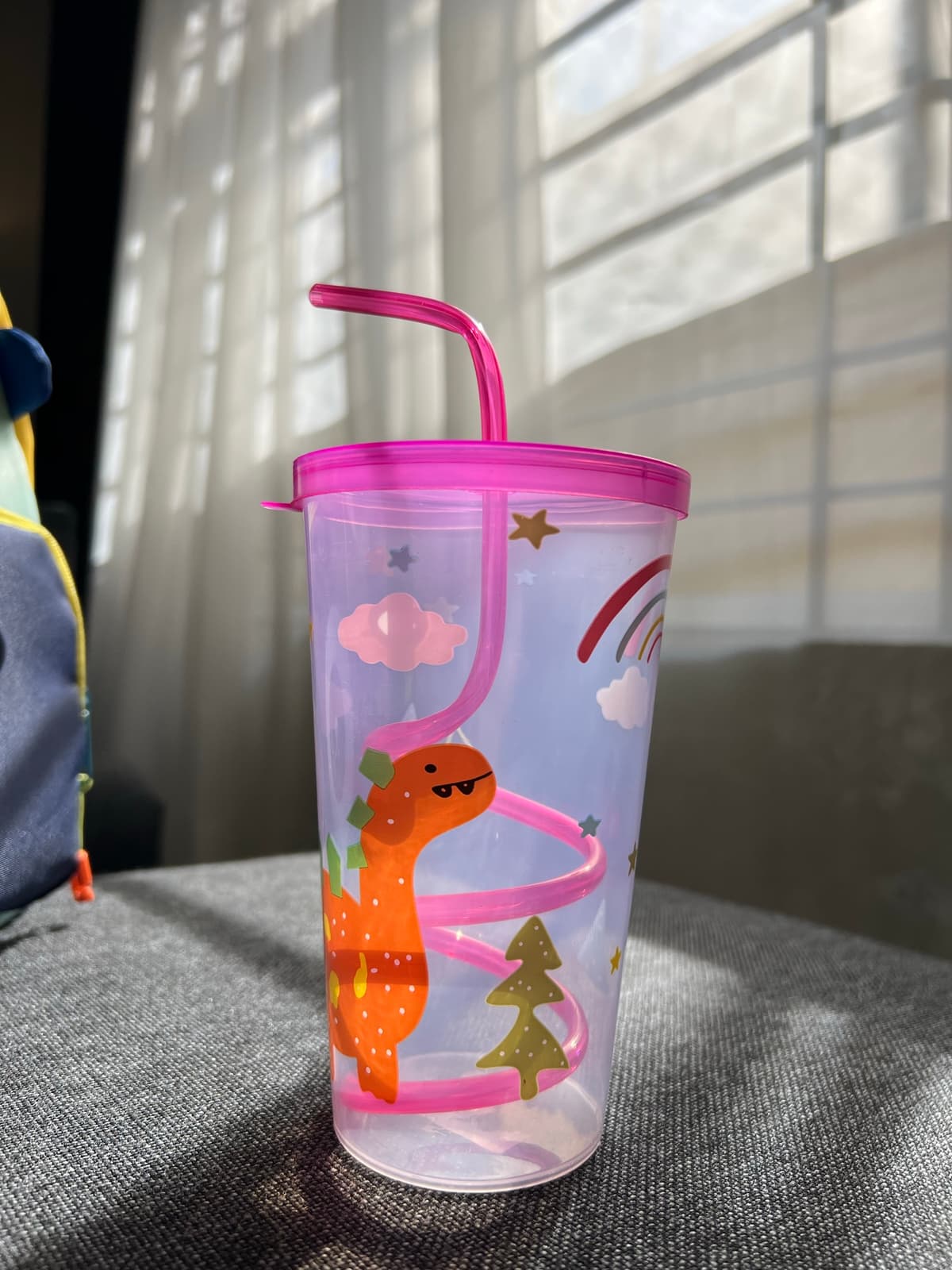 Clear 600 ml cup with a pink lid and pink spiral straw, printed with an orange dinosaur, clouds and a rainbow