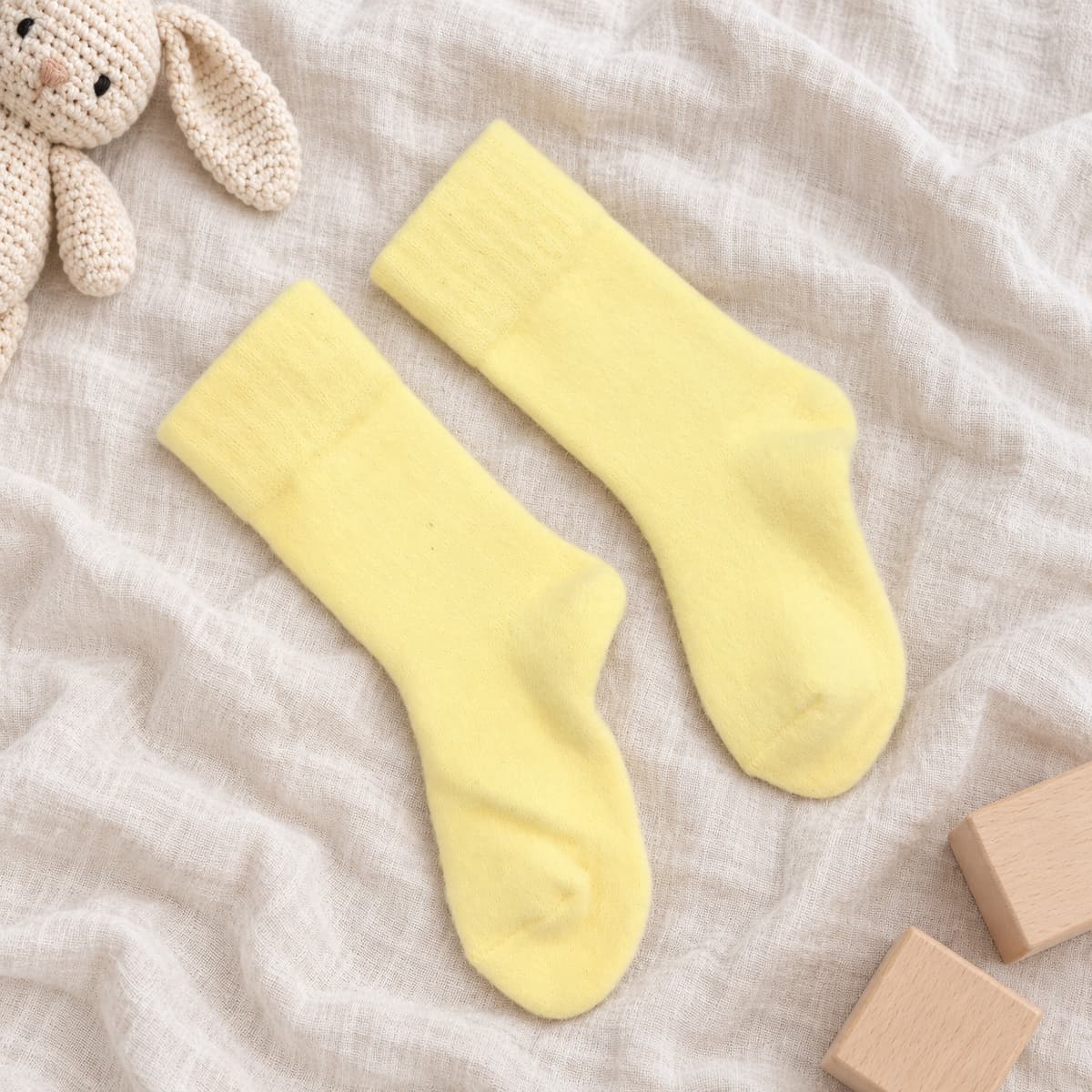 Pale-yellow cotton socks on cream linen with nursery props