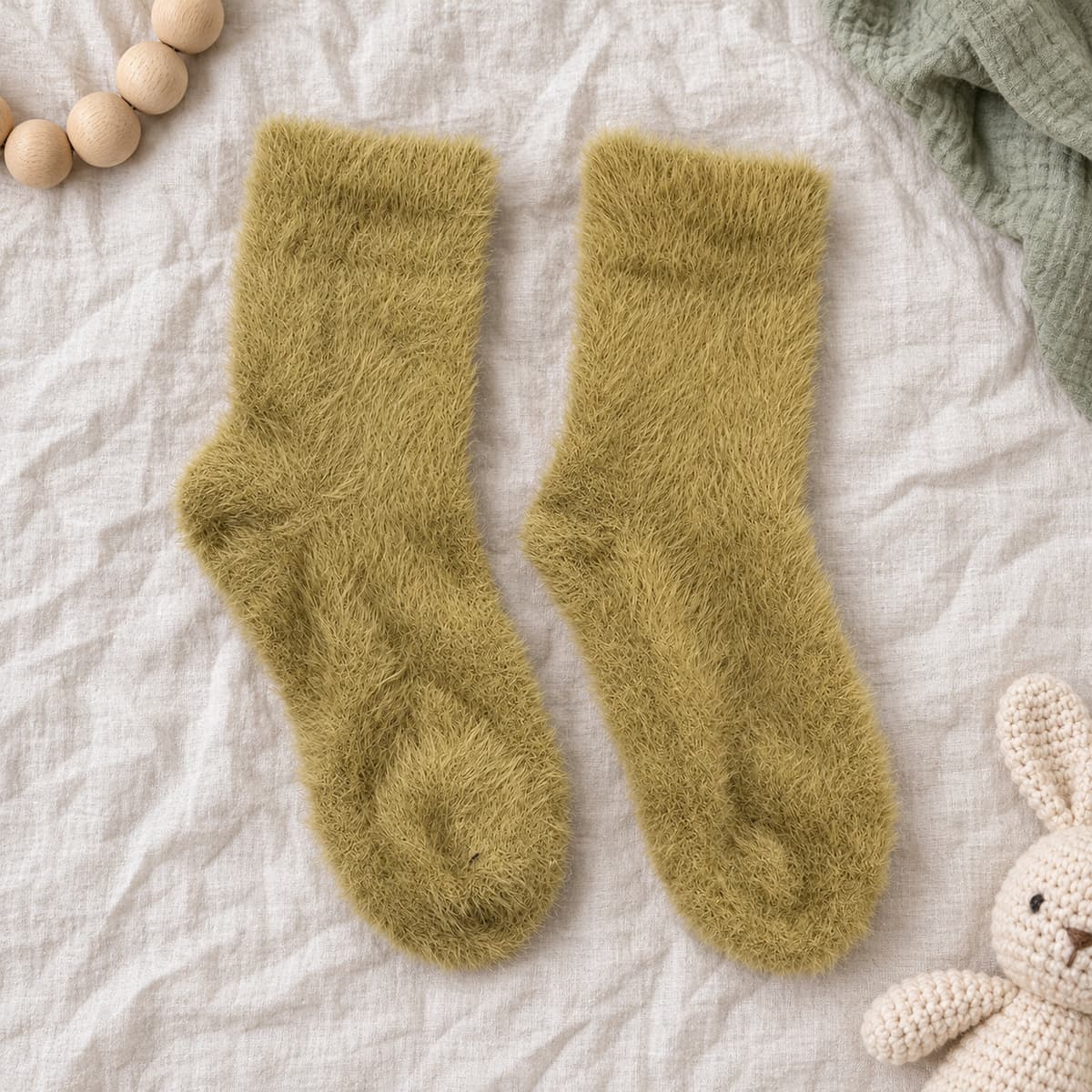 Olive-green furry socks on cream linen with nursery props