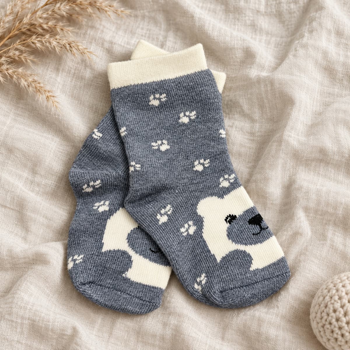 Grey-blue baby socks with paw prints and a bear face on cream linen with nursery props