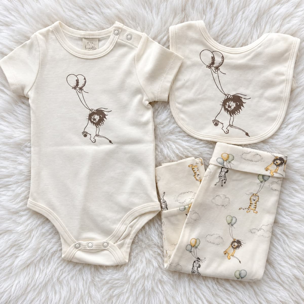 Ivory lion and balloons 3-piece set on white fur: short-sleeve bodysuit, bib and folded printed trousers