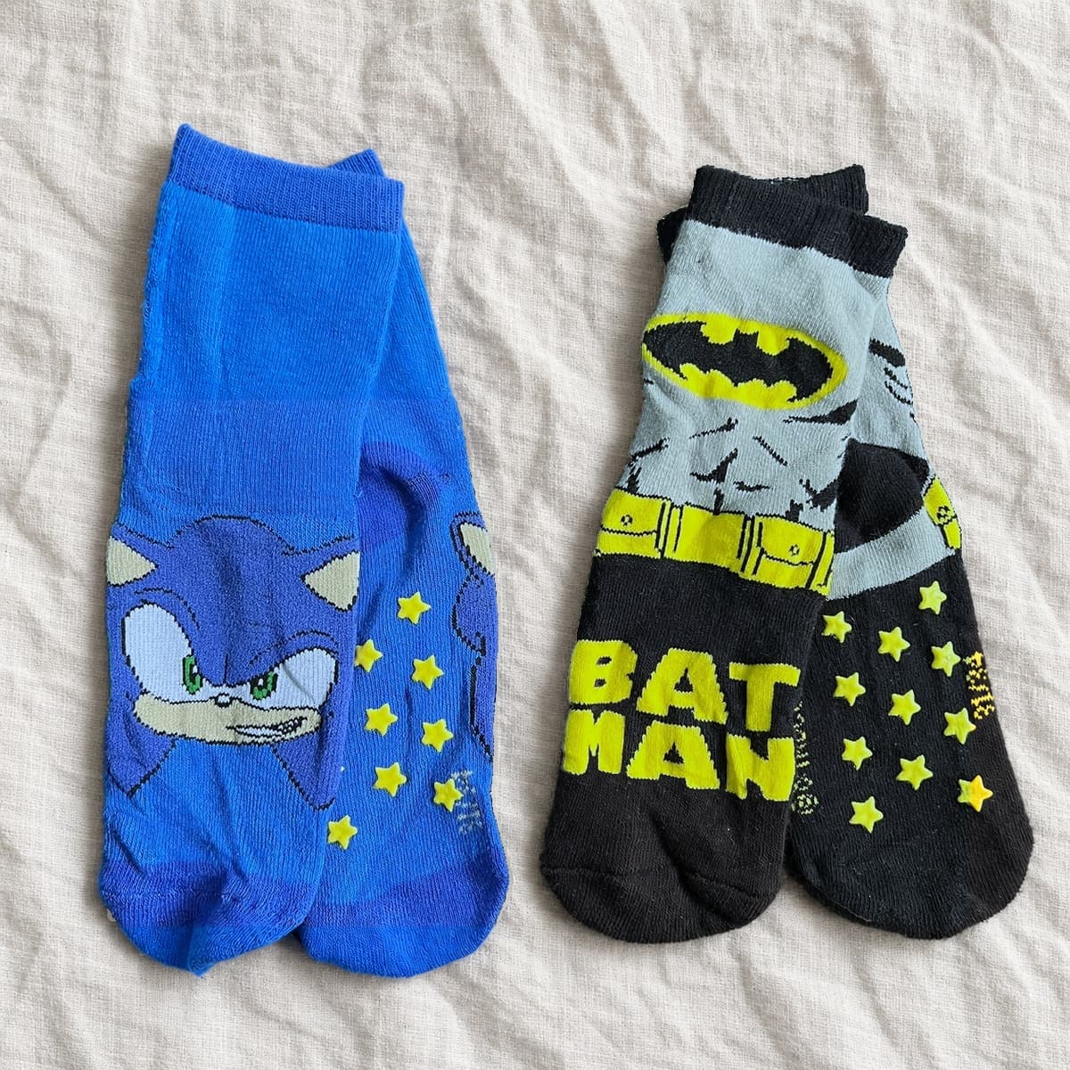 Blue Sonic socks and black and grey Batman socks on linen