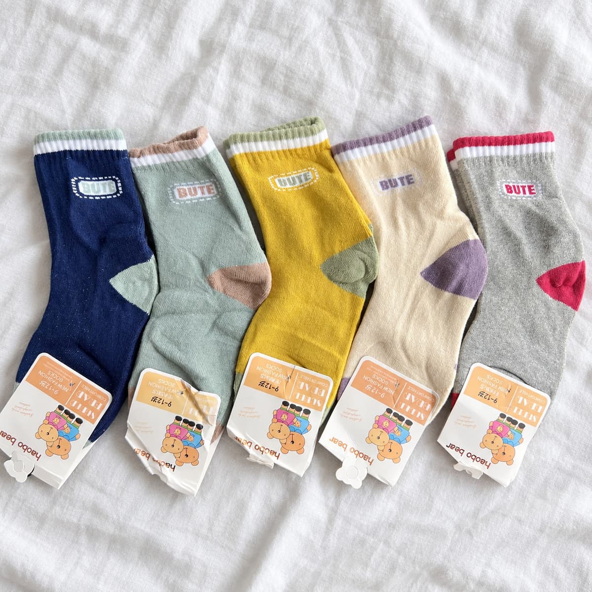 Five pairs of BUTE socks in navy, sage, mustard, cream and grey on cream linen