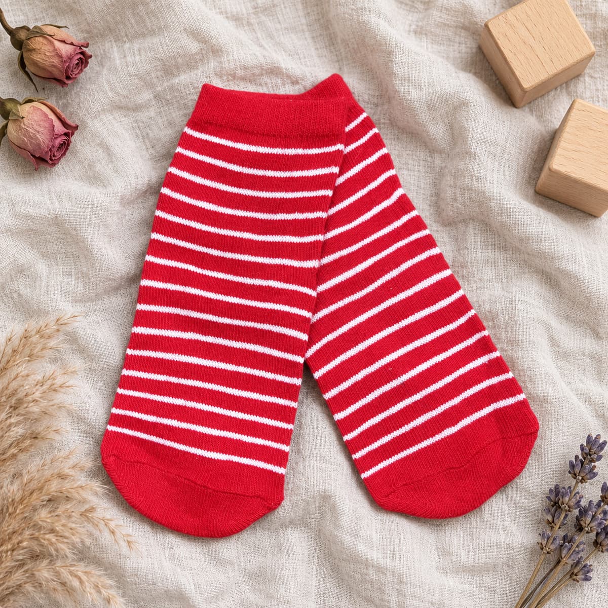 Red ankle socks with thin white stripes on cream linen with nursery props