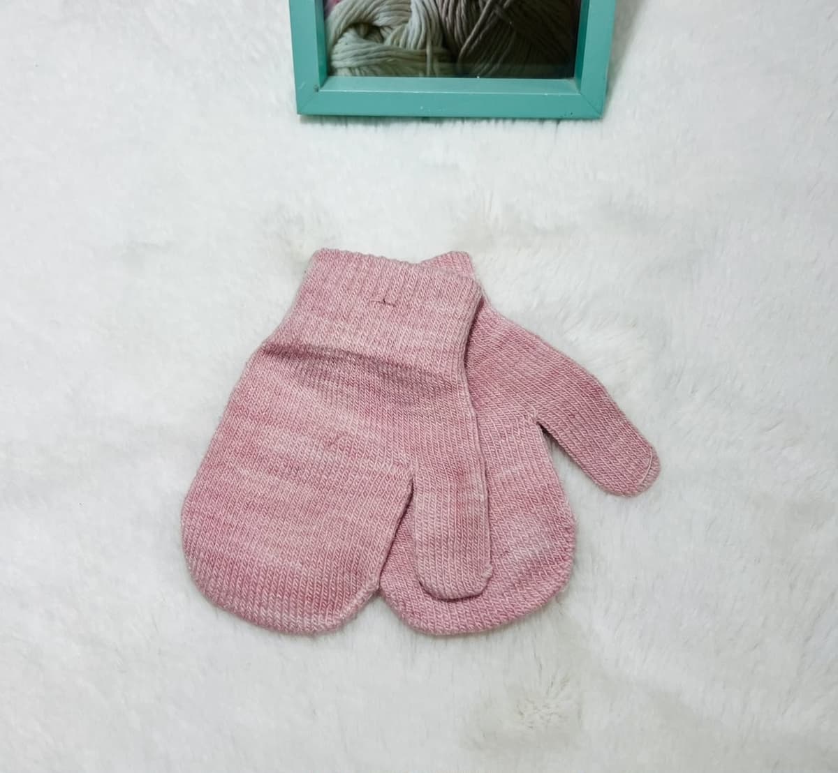 Dusty pink knitted baby mittens on a white fluffy rug
